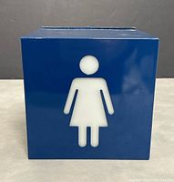 Blue cube with white woman figure symbol on the front, powered off.