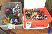 Overview of two plastic bins filled with assorted action figures and toy parts, showing a mixture of characters and toy accessories.
