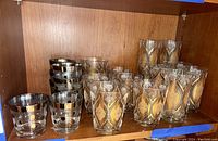 Overall view of both types of vintage glasses placed inside a wooden cabinet, showing quantity and design.