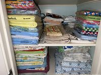 Two shelves filled with stacked linens including folded sheets and pillowcases in various colors and patterns.