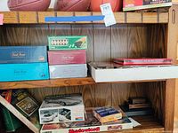 Photo of wooden shelves containing various boxed board games, a chess game box, model car kit, and basketball equipment.