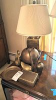 View of brass table lamp and assorted brass decor items on wooden surface.