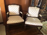 Two Drexel armchairs with light floral-patterned upholstery, ornate carved wood frames and armrests, showing front view on wooden floor.