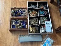 Wooden two-tier box and wooden tray with nine compartments filled with assorted bracelets, necklaces, earrings and brooches, small gray box