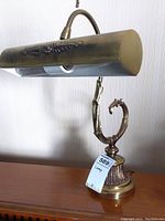Full side view of the antique style metal desk lamp on a wooden surface, showing the curved neck and ornate base.