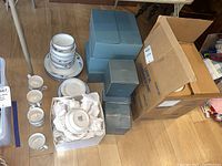 Photo showing stacked Lenox Chinastone bowls, plates, and coffee cups beside original blue Lenox boxes and a cardboard box containing wrapped dishes.
