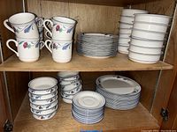 Photo showing stacked coffee cups, saucers, plates, and bowls with floral design inside wooden cabinet.