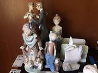 Group photo showing all five Lladro porcelain figurines displayed on shelf, including clown, dancing couple, girl with flowers, and a figurine with three puppies alongside certificate and box.