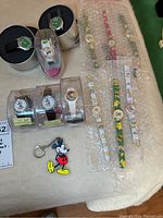 Overview photo showing multiple wristwatches both vintage Lorus Disney-themed watches, colorful fashion watches with cartoon designs on straps, costume jewelry bracelets, and a Mickey Mouse rubber keychain.