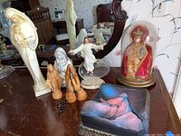 Overview of the lot showing multiple religious figurines including Mary with child statue, small statuettes, rosary beads, dancing Jesus figurine, and the abstract reclining figure statuette