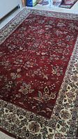 Full view of rug laid flat on floor showing red field and ivory floral border