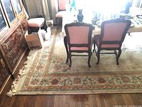 Photo shows the rug under a dining table with chairs in a living/dining room space, displaying its colorful floral border with fringes.