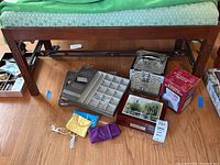 Full view of the settee bench showing wooden frame with carved details and removable cushion with green diamond patterned fabric. Some jewelry and boxes are underneath but not included.