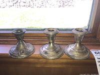 Three weighted sterling silver candle holders side by side on a wooden surface, showing overall shape and size with visible tarnish and wear.