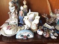 Group shot of entire lot showing variety of figurines, painted wood sign, porcelain and stone items including owls and decorative eggs