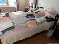 Wide shot of bed covered with stacks of various folded towels and pillows showing various colors and sizes
