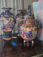 Two porcelain temple jars/vases on a wooden surface showing detailed colorful Asian-themed designs.