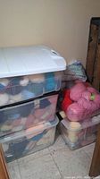 Four plastic bins stacked, filled with assorted yarn balls and skeins in various colors.