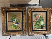 Photo of the set showing both framed paintings side by side depicting tropical birds on large leaves with gold ornate frames