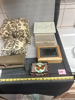 Seven jewelry and trinket boxes arranged on a black and white checkered mat including fabric-covered, wood, metal, and resin boxes.
