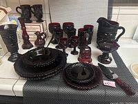 Full lot display of Avon Cape Cod Collection sandwich glass red rosette items including pitchers, glasses, bowls, plates, and accent pieces.