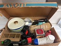 Box containing various vintage Avon bottles and collectibles of various shapes including ceramic boxes and figurine style bottles.