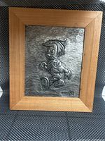 Full view of the framed metal relief artwork of Pinocchio showing wood frame and silver embossed metal.