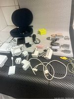 Photo of multiple electronic devices and accessories including charging adapters, flash drives, and cables laid out on a black and white textured surface