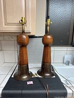 Pair of matching vintage style wood turned table lamps with wide brass bases standing on a kitchen counter in natural indoor lighting.