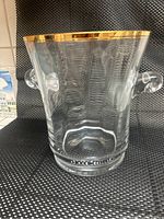 Front view of the clear glass ice bucket with gold rim and handles on a black and white textured surface.