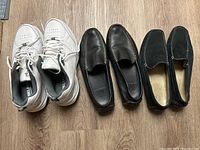 Top down view of three pairs of men's size 13 shoes: white tennis sneakers, two pairs of black loafers.