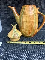 Corn cob shaped coffee pot with lid, showing intricate corn kernel texture and corn-shaped knob on lid. Measuring tape shows approximate width of 11 inches from spout to handle.