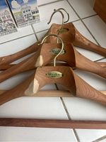 Close-up photo showing three Woodlore cedar wood hangers with metal hooks and Woodlore branding plaques visible on each, highlighting wood grain and condition.