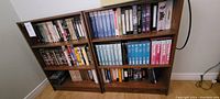 Two brown melamine bookshelves filled with VHS tapes arranged on shelves, showing the range and quantity of tapes included.