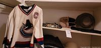Front view of Vancouver Canucks hockey jersey on hanger, with slippers, scarf and hat on shelf