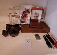Overview of all lot items including wallet, lighter, sunglasses, note books, pens, wooden jewelry holder and decorative boxes