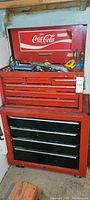 Frontal view of red two-piece steel tool chest with top compartment open, showing tools inside
