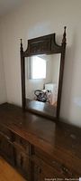 Full view of the wooden dresser with attached tall mirror featuring carved wood details and finials at top.