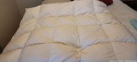 White queen size duvet with a square quilting pattern spread out on a bed, showing overall condition and minor stains.
