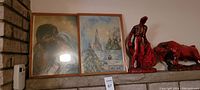 Two framed prints next to a red matador statue and a red bull statue on a mantle against a brick wall and adjacent wall.