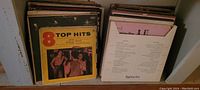 Two shelving units filled with vintage vinyl LP albums and 45 RPM records, showing various album covers including compilation titled '8 Top Hits'.