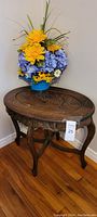 Full view of vintage wood occasional table with embossed oval top and flower arrangement on top
