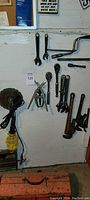 Wall of assorted hand tools including wrenches, ratchets, pipe wrenches, and pliers hanging on a wall.