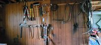 Wide shot showing a variety of garden and hand tools mounted on a wooden wall including saws, loppers, axes, clamps and ropes.