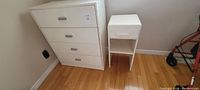 Photo showing full view of white melamine dresser and small white end table on a hardwood floor.