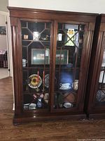 Front view of the dark wood display cabinet showing glass doors with wooden lattice and displayed items inside.