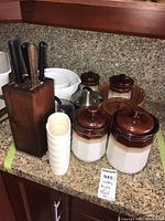 Overview of ceramic canisters, plastic bowls, wooden knife block with knives, and ceramic bean pot on countertop.