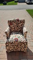 Front view of upholstered armchair showing needlework floral pattern, beige background.