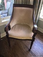 Front view of the wood-framed chair with beige upholstery showing curved arms and carved details on front legs