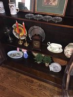 Full view of multiple items on shelves including plates, clock, candlestick holders, pitcher, and small plants